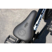 Close-up of Sunday Scout 20" bike black pivotal seat with embossed logo and nearby pedals