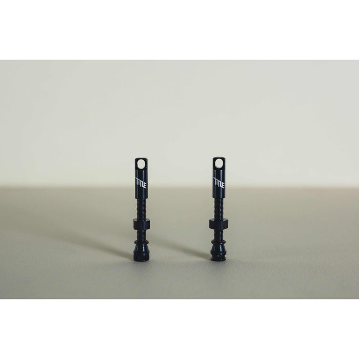 Pair of black MTB tubeless presta valves with double air duct and metal caps on neutral background