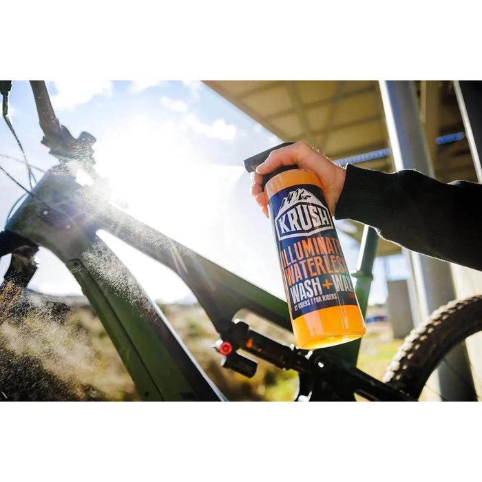 Hand spraying KRUSH Illuminate Waterless Wash on a mountain bike frame outdoors