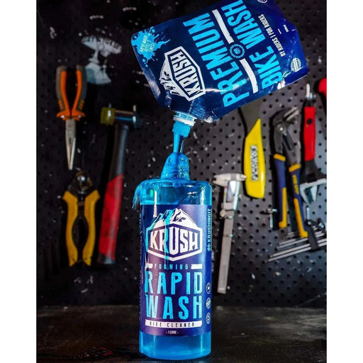 KRUSH Premium Bike Wash Pouch pouring bike cleaner concentrate into bottle in workshop with tools in background