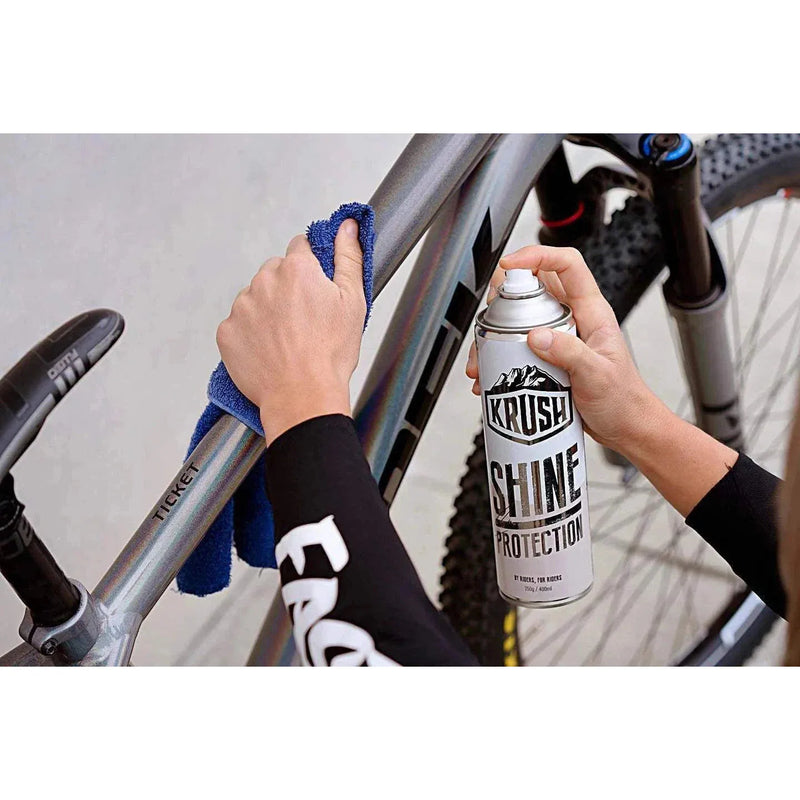 Person applying KRUSH SHINE PROTECTION SPRAY on a bicycle frame with a cloth.