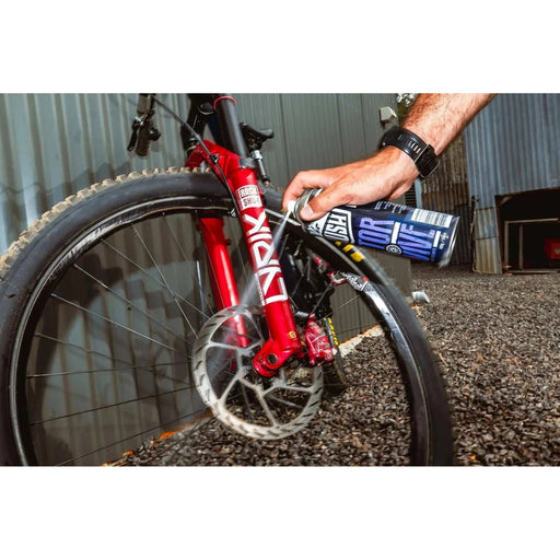 Person applying KRUSH ROTOR REVIVE spray to clean and restore a mountain bike brake rotor.