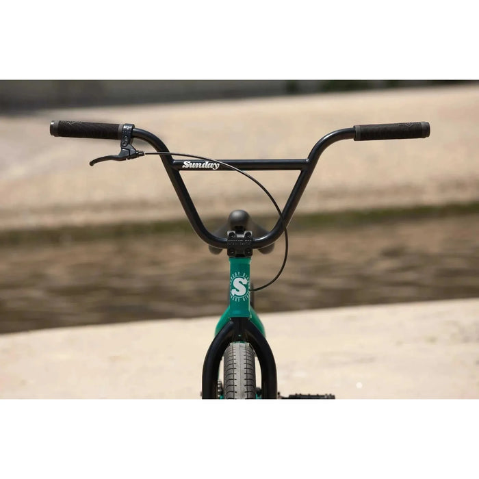 Front view of a Sunday Primer 20" BMX bike with black handlebars and green frame in an outdoor setting.