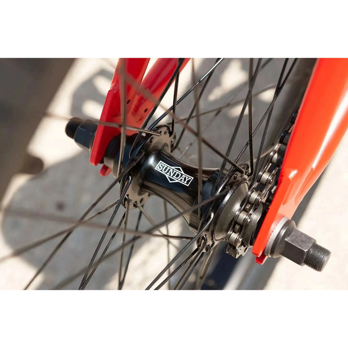 Close-up of the Sunday Primer 20" BMX bike’s black sealed cassette rear hub with red frame fork and black spokes