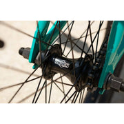 Close-up of black Sunday Primer 20-inch sealed cassette hub on teal bike frame with spokes and chain.