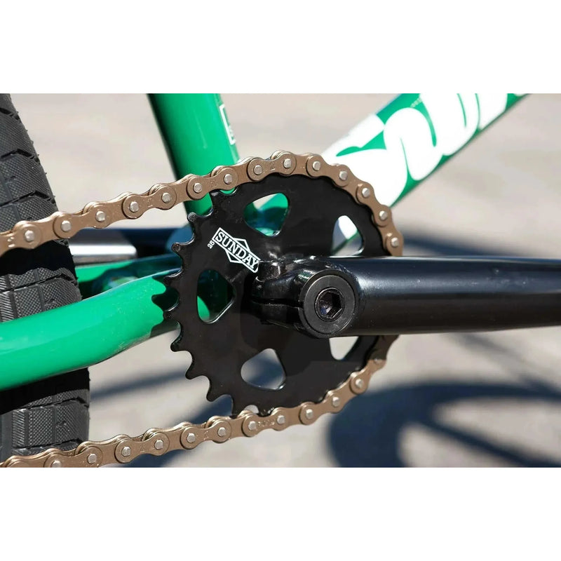 Close-up of Sunday Forecaster BMX bike black sprocket and chain on green frame with crank arm