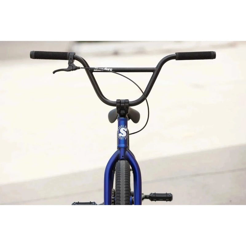 Front view of blue Sunday Model C 24" BMX complete bike with black handlebars and grips against a blurred background