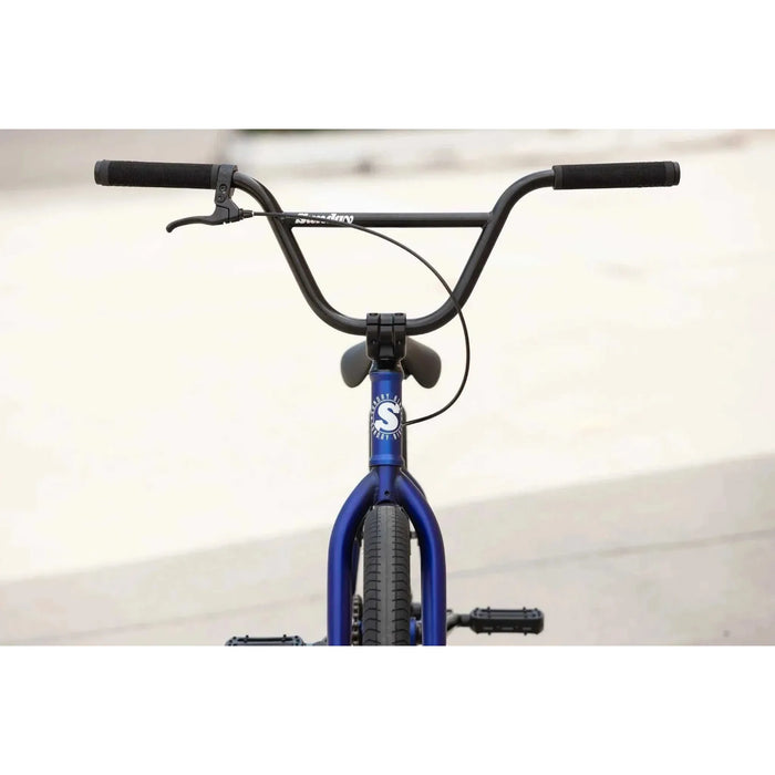 Front view of blue Sunday Model C 24" BMX complete bike with black handlebars and grips against a blurred background