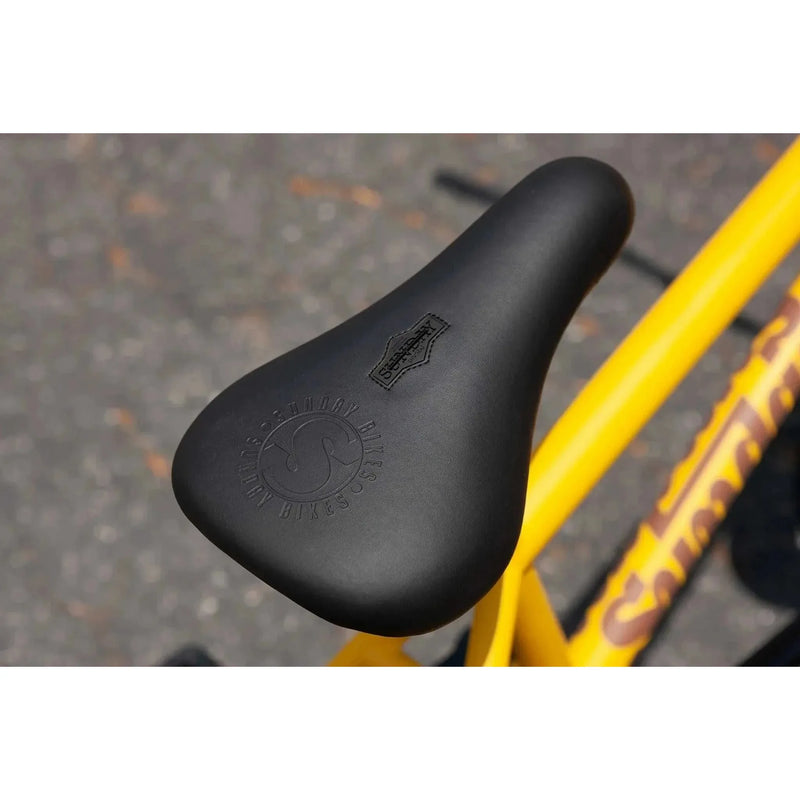 Black BMX saddle with embossed Sunday Bikes logo on matte mustard Sunday EX Arteaga frame