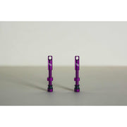 Pair of purple MTB tubeless presta valves with double air duct and metal caps on a beige background