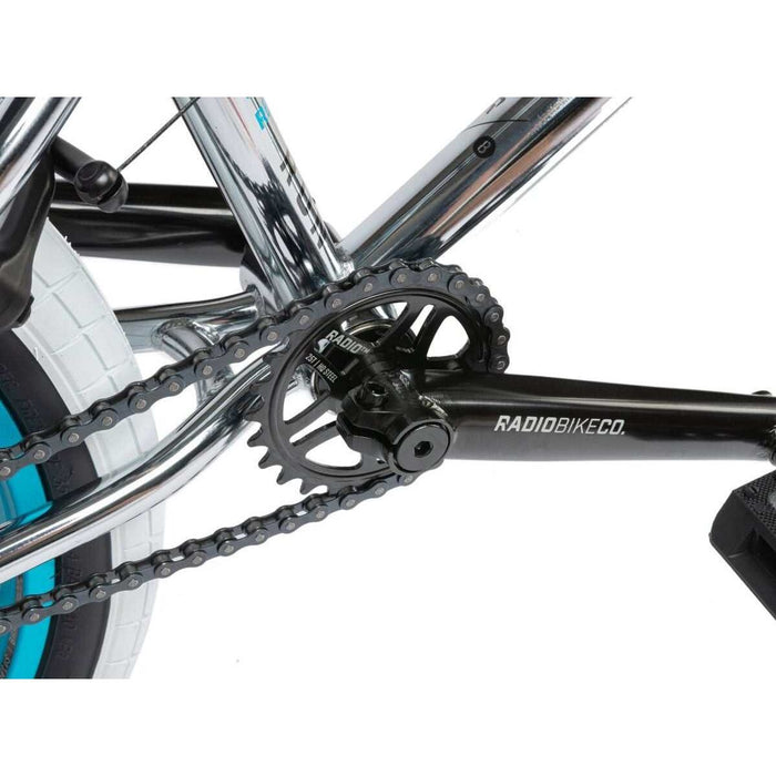 Close-up of RADIO ASTRON FS COMPLETE BIKE crankset and chain with black RADIOBIKECO crank arm and chrome frame.