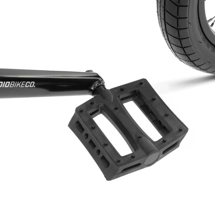 Close-up of black RADIO DARKO bike pedal and crank arm with tire in background on white background