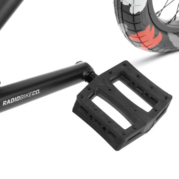 Close-up of black RADIO DARKO bike pedal, crank arm, and rear wheel with red and black tire details.