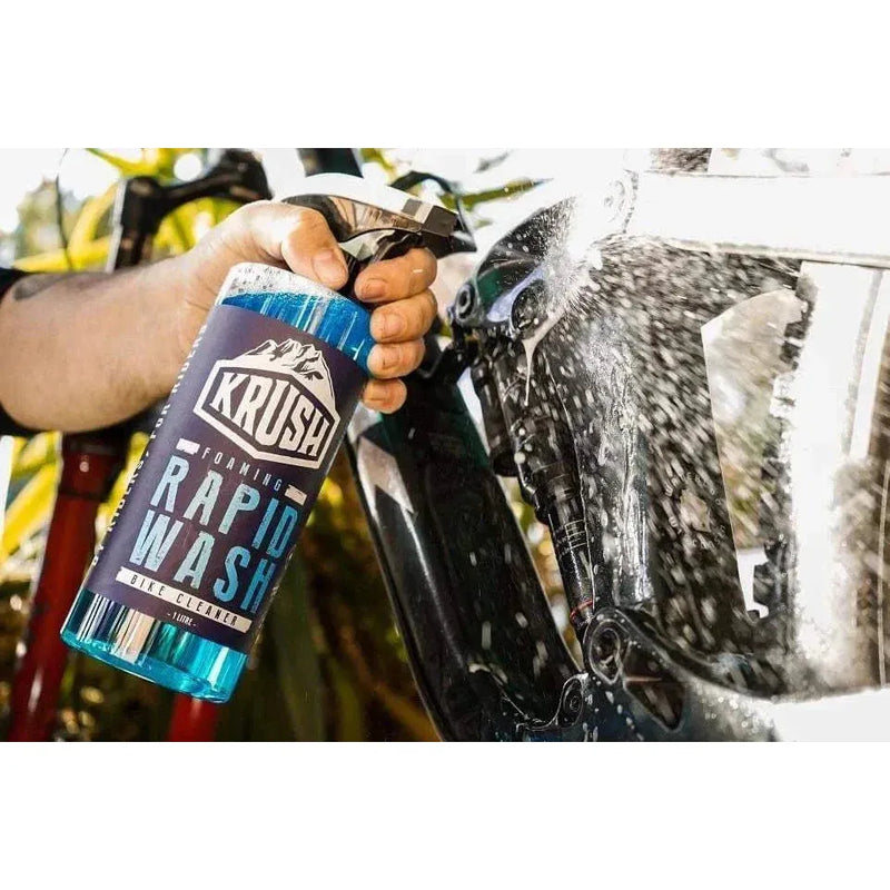 Hand spraying KRUSH RAPID WASH foaming bike cleaner on bicycle frame outdoors