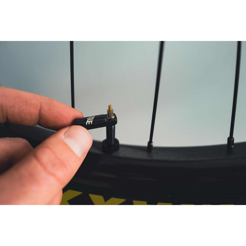 Close-up of a hand installing a MTB tubeless valve on a bicycle wheel rim with spoke details.