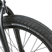 Close-up of WETHEPEOPLE JUSTICE BIKE front wheel with black tire and detailed branding on rim and fork