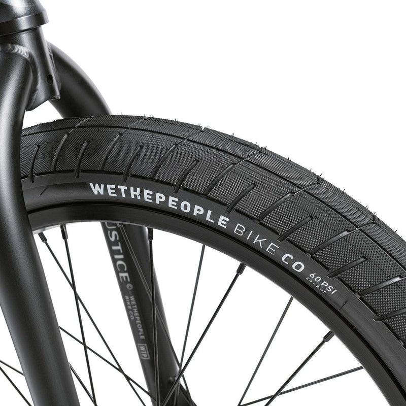 Close-up of WETHEPEOPLE JUSTICE BIKE front wheel with black tire and detailed branding on rim and fork