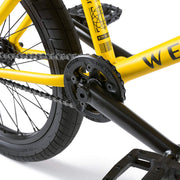 Close-up of the yellow WETHEPEOPLE JUSTICE BIKE showing black crankset, chain, and rear wheel with Activate tire and Paragon sprocket.