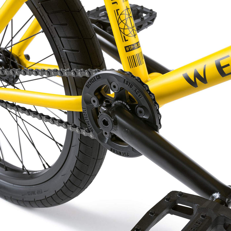 Close-up of the yellow WETHEPEOPLE JUSTICE BIKE showing black crankset, chain, and rear wheel with Activate tire and Paragon sprocket.
