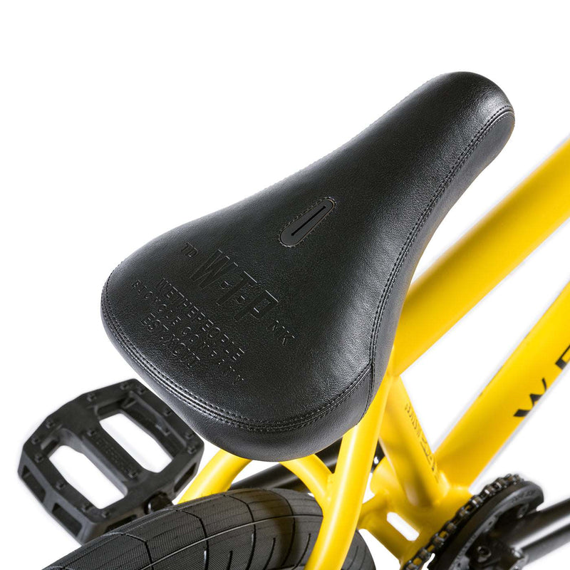 Close-up of black seat, pedal, and yellow frame of the Wethepeople Justice complete BMX bike