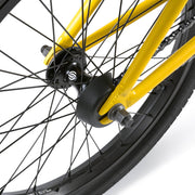 Close-up of the yellow WETHEPEOPLE JUSTICE BIKE rear wheel with black hub, spokes, and plastic hub guard.