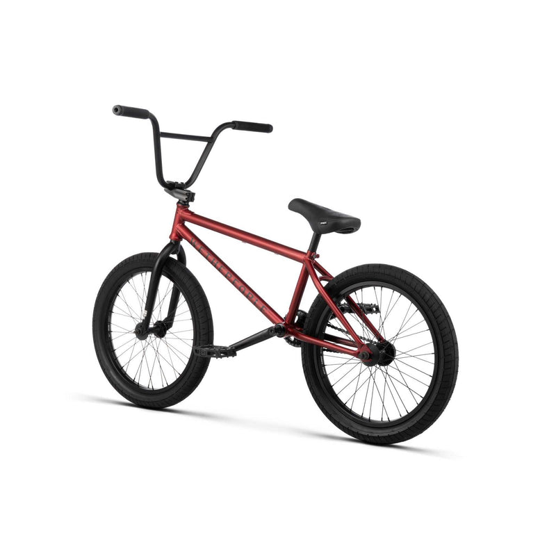 Red Wethepeople Justice bike with black tires, black handlebars, and a padded black seat, designed for urban BMX riding.
