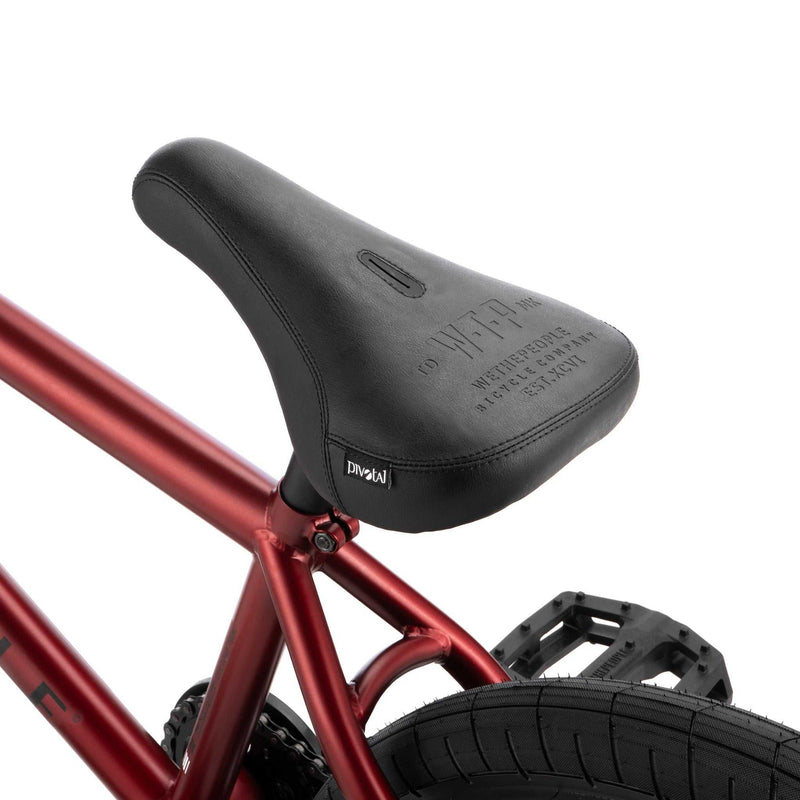 Close-up of black seat and red frame on WETHEPEOPLE JUSTICE BIKE with rear tire and pedal visible