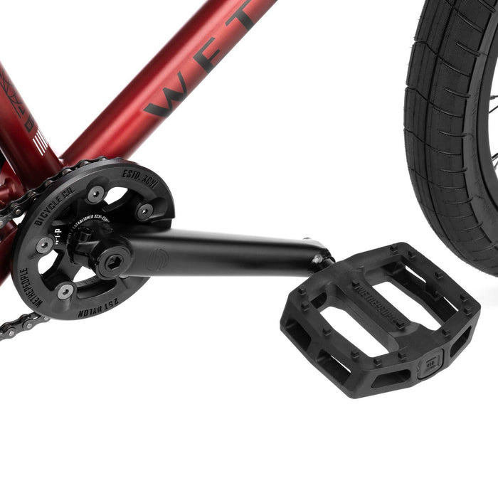 Close-up of Wethepeople Justice Bike's black crankset and pedal with red frame and black tire.