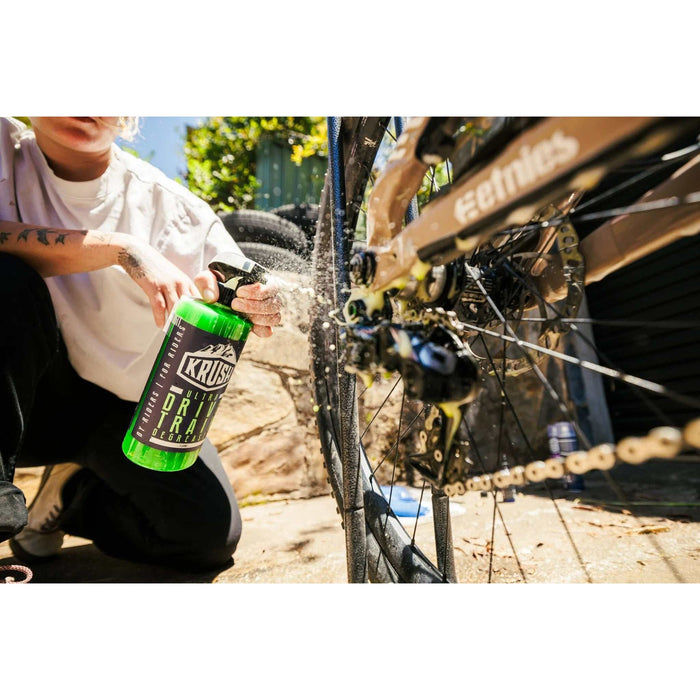 Person using KRUSH ULTRA drivetrain degreaser spray on bicycle chain outdoors