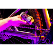 Person applying KRUSH LUSH wet lube to bike chain near rear tire in colorful lighting