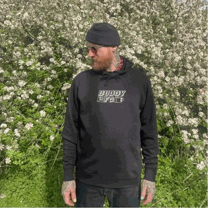 Man wearing black MARIE JADE x BUDDY MFG embroidered hooded sweater with kangaroo pocket outdoors