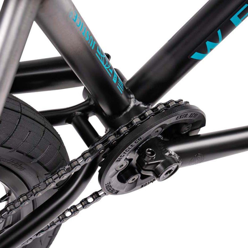 Close-up of the Wethepeople Justice bike's drivetrain featuring the black Paragon Plastic Guard sprocket and chain on a matte black frame with blue logo.